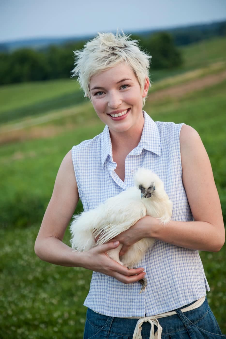 Une éleveuse souriante porte une poule Soie blanche